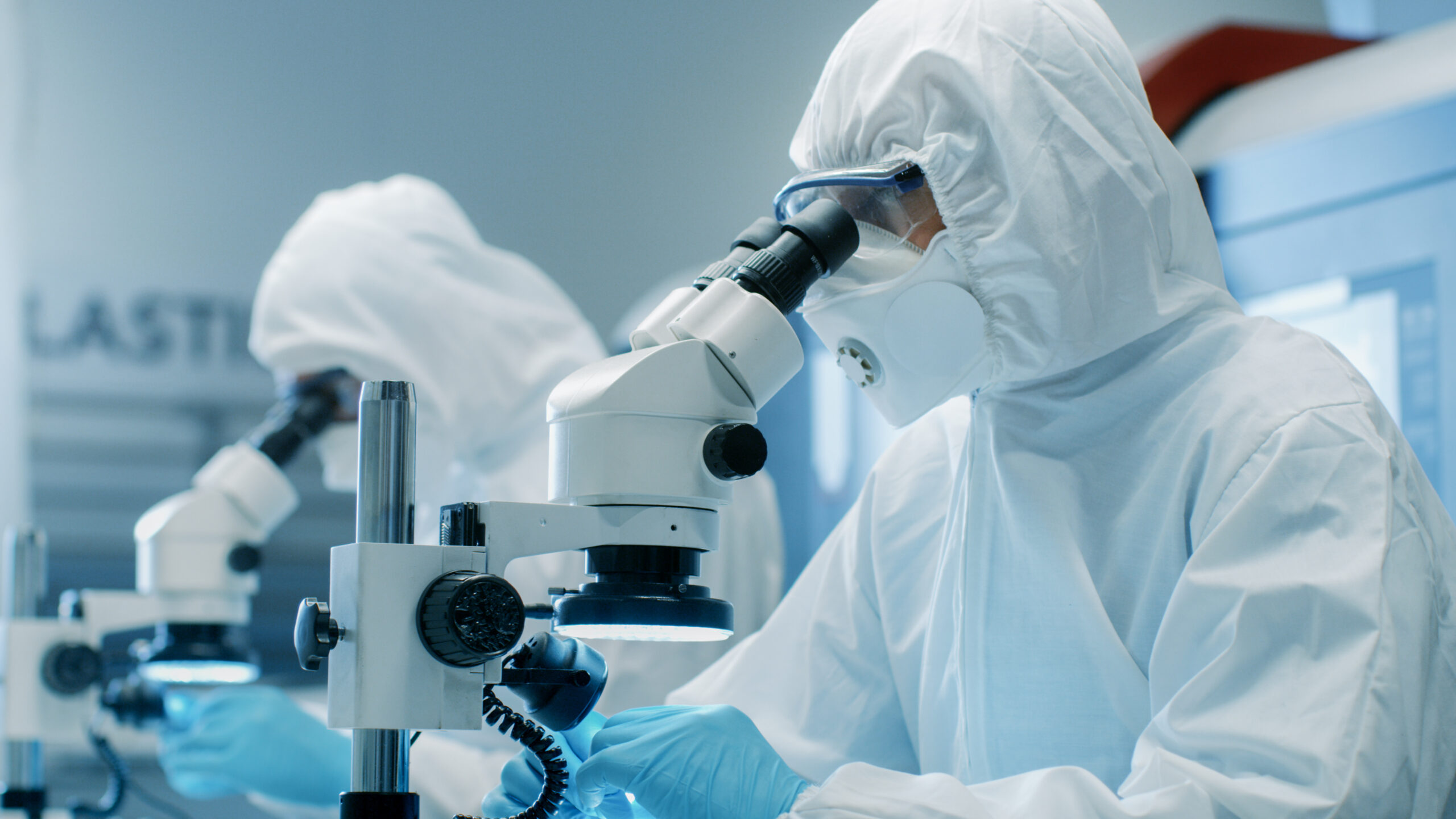 Two Engineers/ Scientists/ Technicians in Sterile Cleanroom Suits Control Manufacturing Machinery Work and Use Microscopes for Component Adjustment and Research. They Work in an Electronic Components Manufacturing Factory.